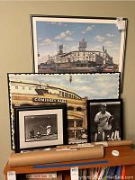 Framed large color poster of Comiskey Park with other framed posters stacked behind and baseball memorabilia in front