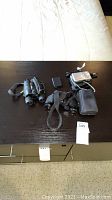 Overview of lot showing three binoculars and digital camera with accessories on dark wood surface