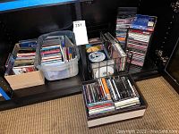 Wide shot showing multiple stacks and boxes filled with various music CDs in jewel cases and plastic containers on a carpeted floor.