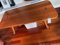 Wooden coffee table viewed from an angle showing top and one side with natural wood finish and turned legs.