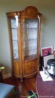 Full view of the wooden display cabinet showing curved glass doors and sides, standing on four carved legs with a decorative top crown.