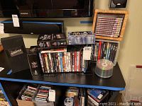 Photo showing various DVD box sets and DVDs including Frank Sinatra in Hollywood, Twilight Zone series, other movie and documentary titles, and stack of blank media discs on a spindle.
