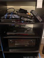 Shelf with multiple electronics devices stacked: Sony players on top two shelves, Denon AV receiver on lower shelf