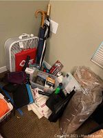 Photo shows a white and gray box fan, umbrellas with wooden and straight handles, a vintage cassette recorder, flashlights, black and blue storage cases, and other miscellaneous items including battery packs and a brown Umbra box frame.