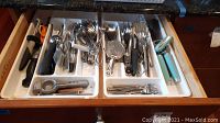 Wide view of the drawer with various metal and plastic kitchen utensils organized in white plastic tray compartments