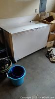 Full view of the white Frigidaire chest freezer with lid closed and surrounding area showing boxes and other household items.