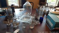 Photo showing assortment of glassware on table including drink dispenser, serving dish, candleholders, swans, and various glasses