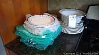 Left stack of shallow plates and bowls wrapped in bubble wrap beside a right stack of plates and bowls in Spisa-Ribb pattern