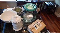 Kitchenware lot on countertop showing several bowls in varying sizes and colors (white, green), a white ceramic compost holder, glass pie pans, and a cardboard box.