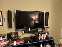 Full wall setup with Samsung TV flanked by two tall Monitor Audio Radius 225 speakers mounted vertically, with a center speaker mounted below the TV, a black console table with DVDs and board games beneath.