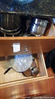 Drawer containing multiple stainless steel pots and pans stacked, alongside metal lids and an inner steamer basket.
