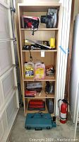 Photo of wooden shelving unit with assorted tools and supplies including drills, circular saw, vacuum, automotive liquids and tool sets