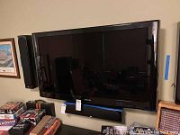 Samsung 46-inch flat screen TV mounted on the wall with wall mount, black frame, soundbar beneath TV, and various other objects around.