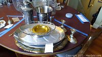 Photo showing large oval silver-tone serving tray, smaller round ridged metal tray, wire basket with golden dish inside, two candleholders, and metal pitcher.