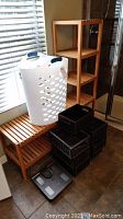 Photo of wood shelving unit with four levels beside white plastic laundry basket, three black baskets stacked, and a digital scale on floor.