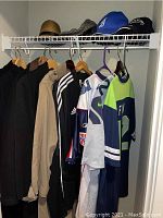 Closet view showing multiple jackets, sports jerseys, and hats on shelf above