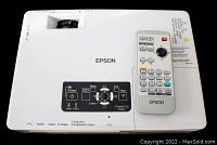 Top view of white EPSON Powerlite 1705c projector with remote control resting on it; the projector shows buttons and ports on top.