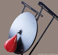 Side angle showing the 24 inch diameter black platform mounted on a heavy duty adjustable black metal frame holding a red Everlast speed bag attached at center.