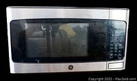 Front view of General Electric microwave showing stainless steel and black exterior, glass window door, keypad on right side.