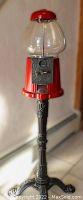 Full view of the red gumball machine on its ornate metal stand showing overall height and structure.