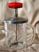 Glass measuring cup marked with cup measurements and fitted with stainless steel lid with nut chopping blades and red handle.