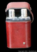 Front view of brown leather travel case open showing two clear glass flasks with metal caps inside.