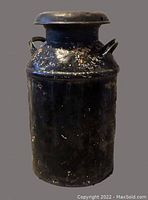 Front view of a black metal milk can with handles and a patina surface.
