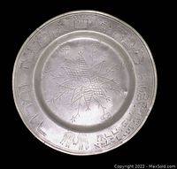 Top view of the round metal plate with engraved star/flower design in center and symbolic figures around the rim.