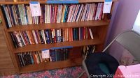 Wooden bookcase filled with books shown from front view in room corner