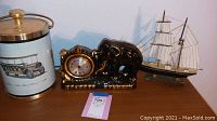 Photo of all three items placed side by side on a wooden surface: the ice bucket on the left, elephant clock in the center, and sailing ship model on the right.