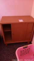 Overall front view of light to medium wood finished mid-century modern cabinet with sliding doors, showing condition and size relative to surrounding objects.