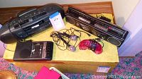 Full overview of the lot showing radios, tape players, microphones and a game controller on a wooden surface.