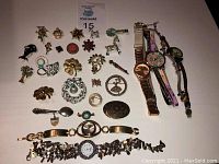 Full view of 25 brooches arranged in rows, and 5 wristwatches on the right side, showing overall assortment and condition.