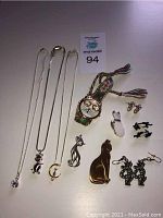 Photo showing all the cat-themed jewelry including necklaces, watch, earrings, and brooches arranged on a flat surface.
