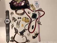 Photo shows an assortment of various cat-themed jewelry including two wristwatches, multiple necklaces, earrings, pendants, a small black cat figurine, and a cat image pouch.