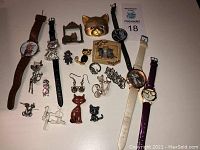 All cat-themed jewelry and watches spread out on flat surface showing variety of items including earrings, pins, brooches, figurines and wristwatches.