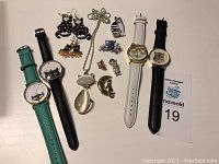 Photo of various cat-themed fashion jewelry items and four wristwatches on a white background. Items include earrings, pendants, brooch pins, rings, and watches with cat designs.