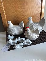 Photo showing four ceramic hen on nest dishes, one painted with red comb and yellow beak, arranged on placemat.