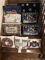 Eight Christmas-themed decorative pillows arranged on wooden steps, shows variety of designs and text.