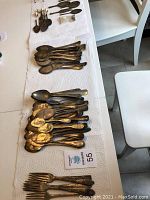 Overview of multiple flattened spoons and forks arranged on paper towel on table surface