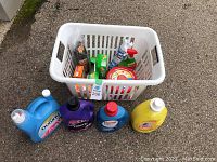 Laundry basket with various brands of laundry detergents and cleaning supplies visible inside and around the basket.