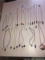 Overview of all 29 pieces: 28 necklaces and 1 pendant in various styles and colors laid flat on white background