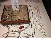Photo showing 12 necklaces laid out with two red rose pins and a locket keychain