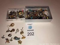 Wide shot showing two boxes filled with various vintage earrings including pierced and clip-ons arranged on a white surface.