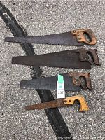 Four old hand saws laid out showing overall size, blade, and handle differences.