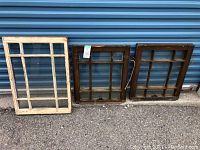 Two old window frames set against a blue door; one white painted frame and one dark brown wooden frame.
