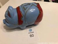 Side view of blue ceramic piggy bank shaped like a pig with red collar and pants, showing gold detailing.