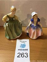 Photo showing two Royal Doulton porcelain figurines on a wooden surface.