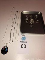 Full lot showing three silver necklaces including one with a glass pendant and six silver rings displayed on a metal tray.