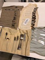 Rolled cloth pouches holding various types of silver plated cutlery including spoons, forks, and knives.